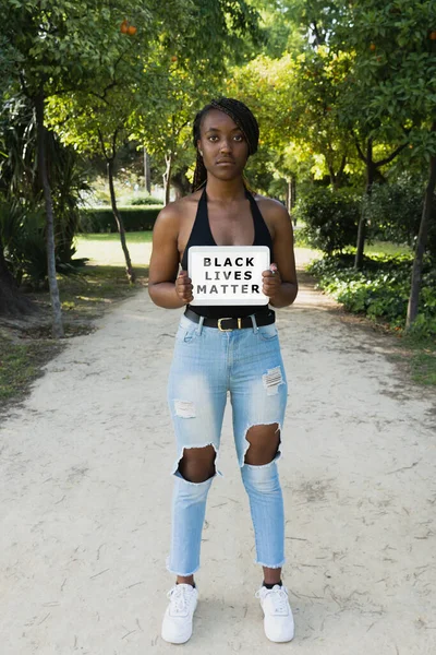 Young African woman with an angry gesture, claiming the human rights of black people with a sign on a tablet.