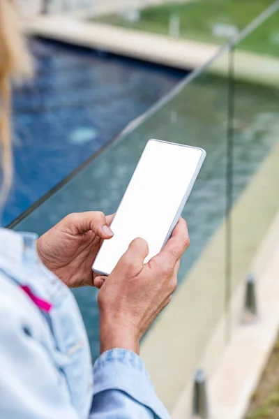 Close-up of a womans hands using a smartphone at the edge of a pool in the background. Vertical photo.