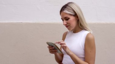 Arka plandaki duvarda cep telefonuyla sörf yapan sarışın bir kız.. 