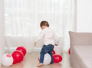 Evinde beyaz ve kırmızı balonları olan sevimli küçük bir çocuk. Sevgililer Günü konsepti. Yumuşak odak.