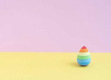 Sarı-pembe arka planda paskalya yumurtası şeklinde kozmetik sünger. Boşluğu kopyala.