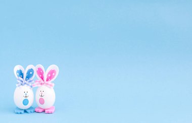 İki beyaz yaratıcı yumurta boyalı gözlü ve çok renkli kulakları ve pençeleri sol köşede mavi bir arka planda..