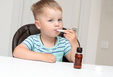 - İnsanlar. Çizgili turkuaz tişörtlü yakışıklı beyaz bir çocuk beyaz bir masada oturur ve şırıngayla ilaç içer. Sağlık konsepti. Yakın plan. Yumuşak odak.