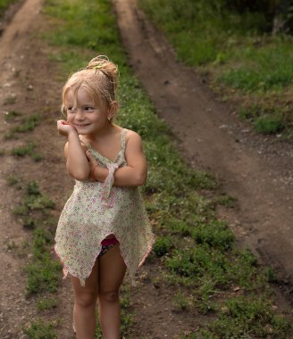 People. Children. A beautiful little and happy Caucasian girl stands on a country road at the dacha in summer and smiles cheerfully. Soft focus. Concept.vertical