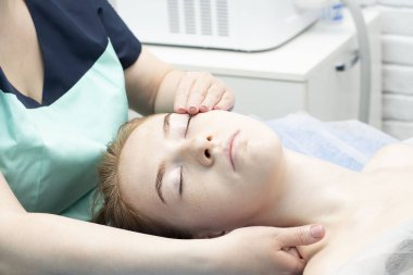 - İnsanlar. Genç, bakımlı, pürüzsüz ve genç yüzlü beyaz bir kız güzellik salonundaki bir kanepede uzanır ve yüz masajı yaptırır. Sağlık konsepti. Yakın plan. Yumuşak odak.