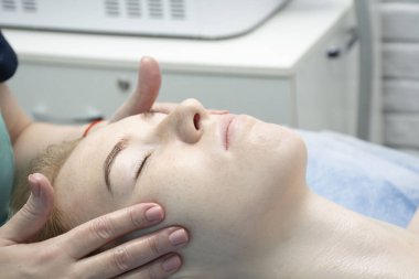 - İnsanlar. Sağlık ve güzellik konsepti. Güzellik salonunda uzman bir kozmetik uzmanı bakımlı, genç ve pürüzsüz yüzlü genç bir Avrupalı kıza stres önleyici bir yüz masajı yapıyor. Yakın plan..