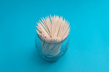 Eşyalar. Kavram. Turkuaz arka planda cam bir fincanda manikür için turuncu tahta çubuklar. Yakın plan. Minimalizm. Yumuşak odaklanma. Boşluğu kopyala.