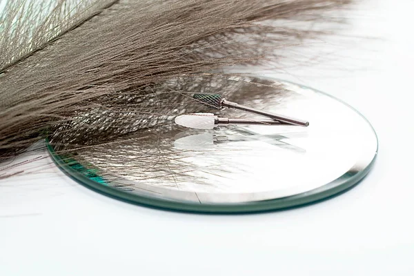 Items. Layout. Two cutters, metal and ceramic, for manicure of nails lie on the mirror next to the decorative feather. Close-up. Soft focus.Concept. Creative.