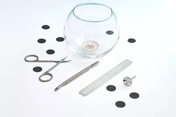 Items. Mock-up of professional metal tools for manicure on a white background. Transparent vase with scented candle. Close-up. Soft focus. Concept.