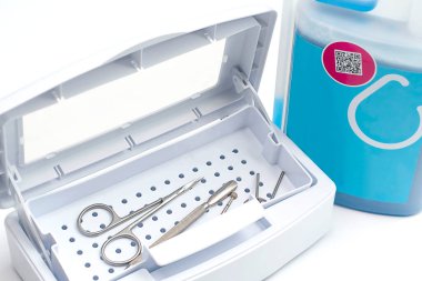 Beyaz plastik bir kapta manikür ve pedikür için profesyonel metal aletler. Sterilizasyon sıvısı. Beyaz arka plan, yakın plan, yumuşak odaklanma. Sağlık kavramı.