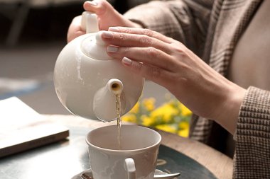 Kadınların elleri açık bir kafede, beyaz seramik çaydanlıktan bir fincana yeşil çay döker. Kavram. Yakın plan. Yumuşak odak.