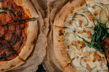 Parşömen kağıdında servis edilen iki farklı pizza. Et ve vejetaryen.