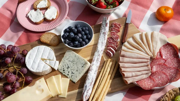 Tahta masada çeşitli peynir ve meyveler var.