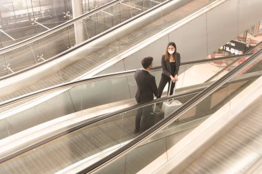 Yürüyen merdivende yüz maskesi takıp sohbet eden iki iş adamı ve kadın Coronavirus veya covid-19 salgınını önlemek için yeni normal insanlar..