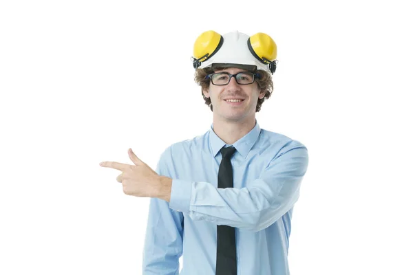 若いエンジニアの男の肖像は ハード帽子の笑顔を身に着けていると立ちながら 孤立した白い背景の上にフレームの左側に空のスペースに指を指す — ストック写真