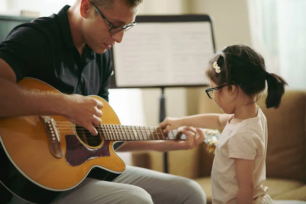 Bebeklerin müzik enstrümanını keşfettikleri sahne, gitar çalan müzik öğretmeniyle birlikte gitar çalan sevimli küçük kız, gitar tellerini denerken. Çocuk beyni gelişimi. Okula geri dön..
