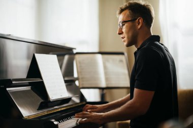 Müzik enstrümanı odasında piyano çalan bir adamın yan görüntüsü