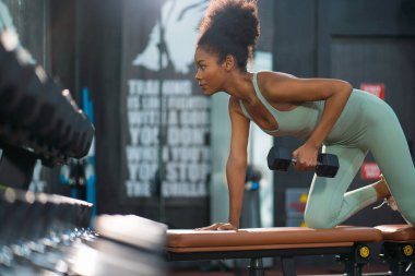 Genç sporcu zenci kadın portresi. Dambıl egzersizini konsantre ve kendinden emin bir ifadeyle kaldırdı. Kadınların kas sağlığı eğilimini azaltmak için yaşam tarzı çalışması.