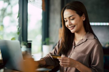 Bilgisayarla online alışveriş yapmak için elinde kredi kartıyla gülümseyen genç bir Asyalı kadın..