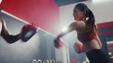 Asyalı genç bir kız spor salonunda koçluk yaparken siyahi bir adamla boks antrenmanı yapıyor. Dayanıklılık eğitimi eğlence aktivitesi. Kızgın kadın boks partneriyle boks eldivenini yumrukluyor..