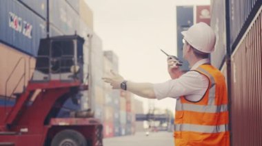 Konteynır deposunda çalışmak için telsiz telsizi kullanarak akıllı, yakışıklı, beyaz, endüstriyel nakliye işçisinin orta boy görüntüsü..