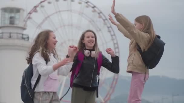 Три Однолітків Шкільними Сумками Щасливо Стрибають Танцюють Біля Парку Розваг — стокове відео