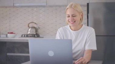 Smiling young blonde woman makes checkout and finishes online purchase with bank card and claps her hands happily.