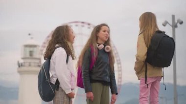 Three school girlfriends hang out after classes near Luna park with Ferris wheel. Girls school friendship concept. High quality 4k footage