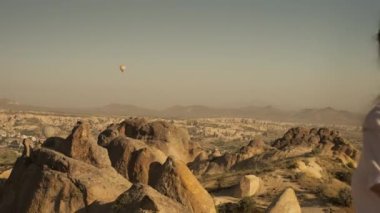 Side view of young woman with long hair in casual clothes and sunglasses admiring scenic landscape of rocky cliffs in Cappadocia valley