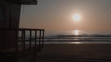 Lifeguard tower silhouette at sunset time on empty beach with moderate waves. Beautiful tranquil slow motion of sea at evening time. High quality 4k footage