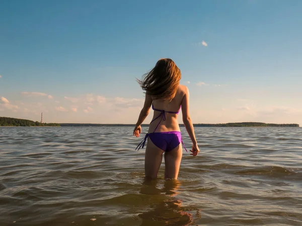 夏の夜の夕日の海のビーチの水の背景に太陽のオレンジ色の光の中でビキニ水着で若い魅力的な女性 美しさと健康の概念 ビーチの休日 日焼け 屋外休暇 — ストック写真