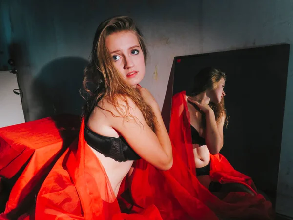 一个年轻美丽的金发女人 戴着红色的面纱 穿着黑色的内衣裤 面对着一面镜子 美丽美丽的女性的身体 妆容和化妆品 呵护身体 — 图库照片