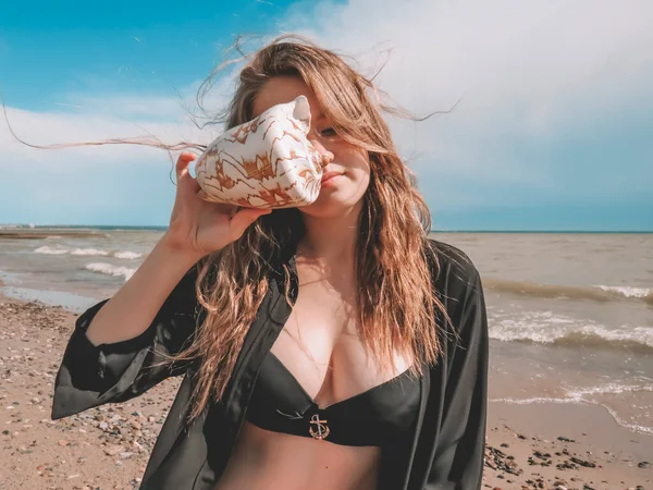 비키니를 머리를 조개껍데기를 셔츠를 여성은 해변에서의 여름날 파도를 배경으로 휴일의 — 스톡 사진