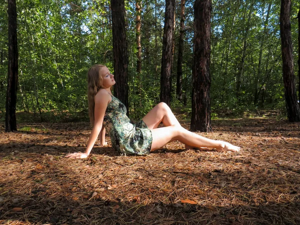 在一个阳光明媚 阳光明媚的温暖夏日 一位红头发 身材苗条 身材苗条 身披紧身衣 光着双肩的年轻女子躺在由落松针叶织成的黄地毯上 沐浴在针叶林的光芒中 — 图库照片