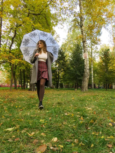在一个阳光灿烂温暖的金色秋天 秋天的风景 西伯利亚金秋的概念 女人的美丽 年轻美丽的金发女郎 身穿灰色羊毛外套 头戴白色敞篷 在城市公园散步 — 图库照片