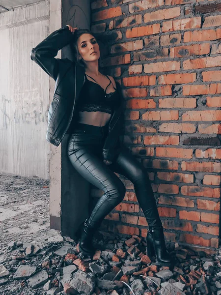 黒の革のジャケットとレギンスと放棄された建物内のレンガの壁に対する黒のブラの上にスリムなボディを持つ若い魅力的な女性 — ストック写真
