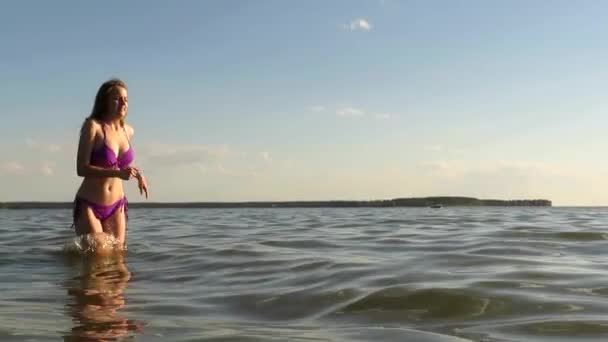 夕日の夏の夜に海の湾の水で実行されているビキニでスリムなボディを持つ魅力的な若い女性 ビーチの休日の概念 アクティブなライフスタイル 海の休日 日焼け 水処理 — ストック動画