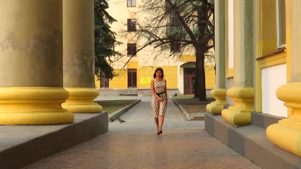 Mladá krásná žena v letních bílých puntíkových šatech na procházce po městě v kolonádě staré budovy při západu slunce, aktivním životním stylu, turistice, cestování a turistice, módě a stylu.