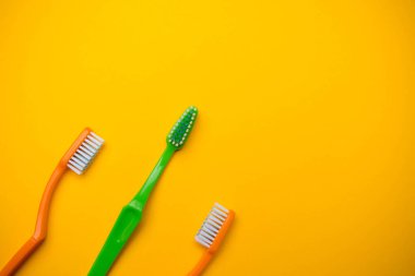 Ağız ve diş sağlığı konsepti sarı arka planda üç diş fırçası gösteriyor
