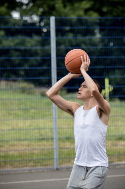 19 yaşında bir ergen çocuk halka açık bir parkta basketbol sahasında şut çekiyor.