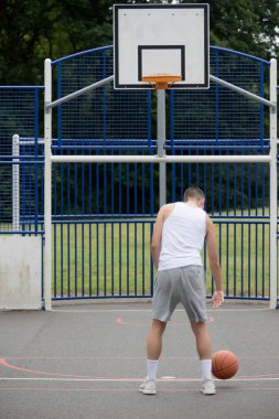 19 yaşında bir ergen çocuk halka açık bir parkta basketbol sahasında şut çekiyor.