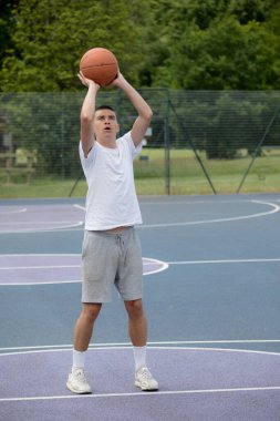 19 yaşında bir ergen çocuk halka açık bir parkta basketbol sahasında şut çekiyor.