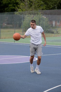 Halka açık bir parkta basketbol oynayan 19 yaşında bir genç çocuk.