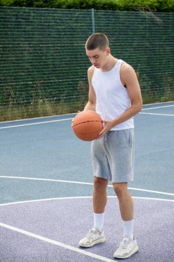 19 yaşında bir ergen çocuk halka açık bir parkta basketbol sahasında şut çekiyor.