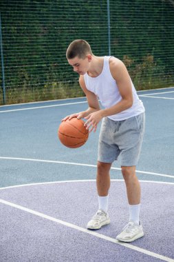 19 yaşında bir ergen çocuk halka açık bir parkta basketbol sahasında şut çekiyor.
