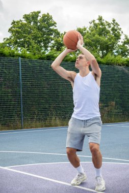 19 yaşında bir ergen çocuk halka açık bir parkta basketbol sahasında şut çekiyor.