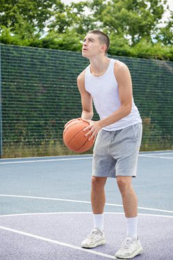 19 yaşında bir ergen çocuk halka açık bir parkta basketbol sahasında şut çekiyor.