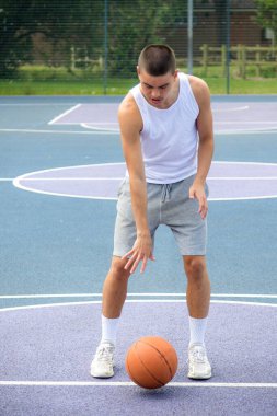 Halka açık bir parkta basketbol oynayan 19 yaşında bir genç çocuk.