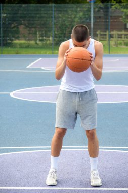 Halka açık bir parkta basketbol oynayan 19 yaşında bir genç çocuk.