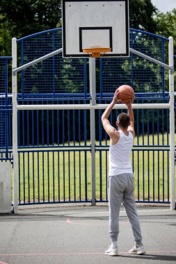 19 yaşında bir ergen çocuk halka açık bir parkta basketbol sahasında şut çekiyor.